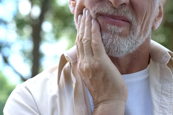 An elder man grasps his jaw in pain
