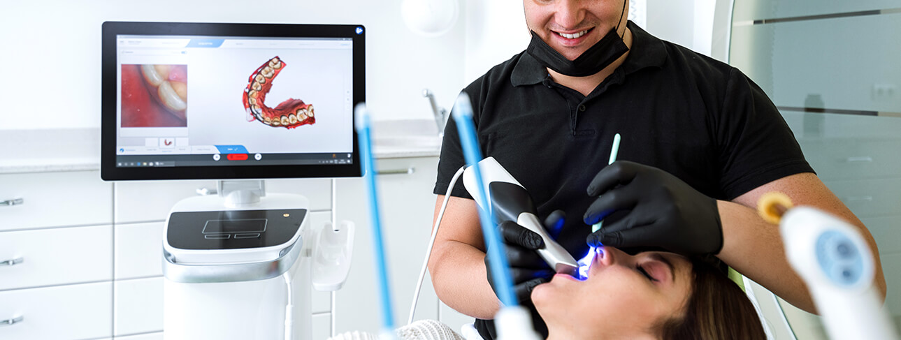 a dentist examining a woman's teeth with a handheld imaging device