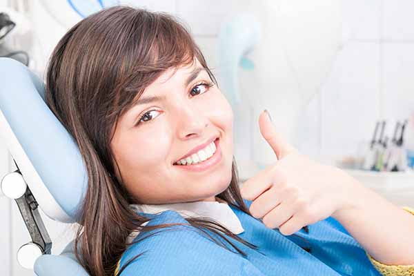 Closeup of brunette female patient smiling and showing thumb up in dentistry and being relaxed