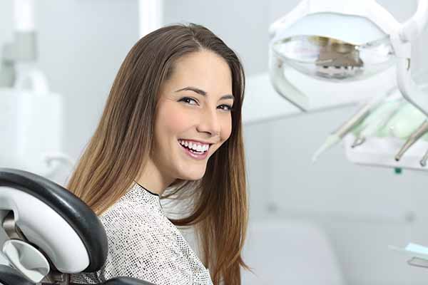 Satisfied dentist patient showing her perfect smile after treatment in a clinic box with medical equipment in the background